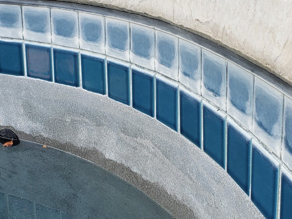 Water in pool has been drained to reveal 20 year old calcium deposits. The lower row of tiles have been resurfaced and look brand new.